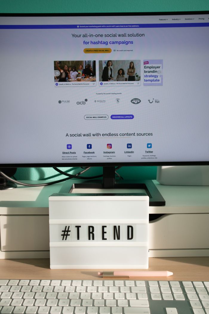 project-03-b A clean and modern desk setup with a lightbox displaying #TREND and a computer monitor showing a social wall solution.